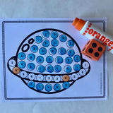 a white worksheet on a white background with a clip art planet. It was dozens of circles fill with numberals. An orange dot marker and foam dice lay next to the dot marker worksheet